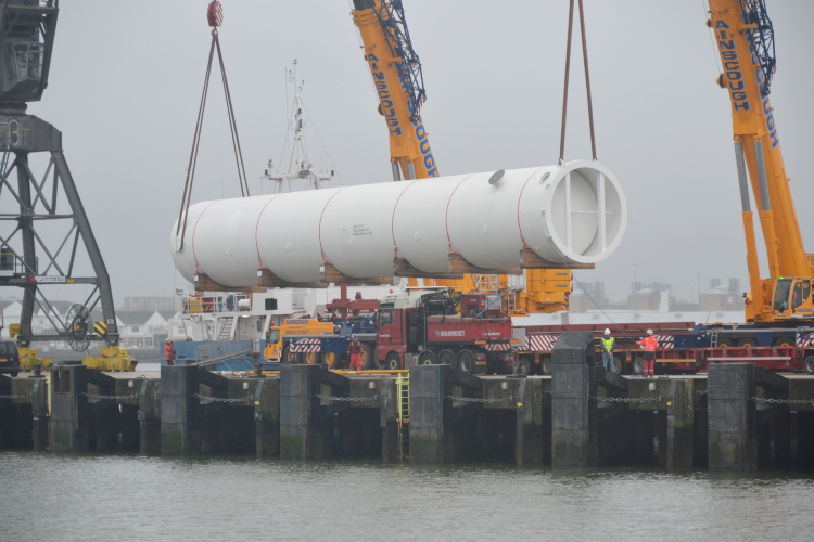 a large white tube being lifted onto a vehicle by cranes