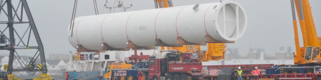 a large white tube being lowered onto a vehicle with cranes